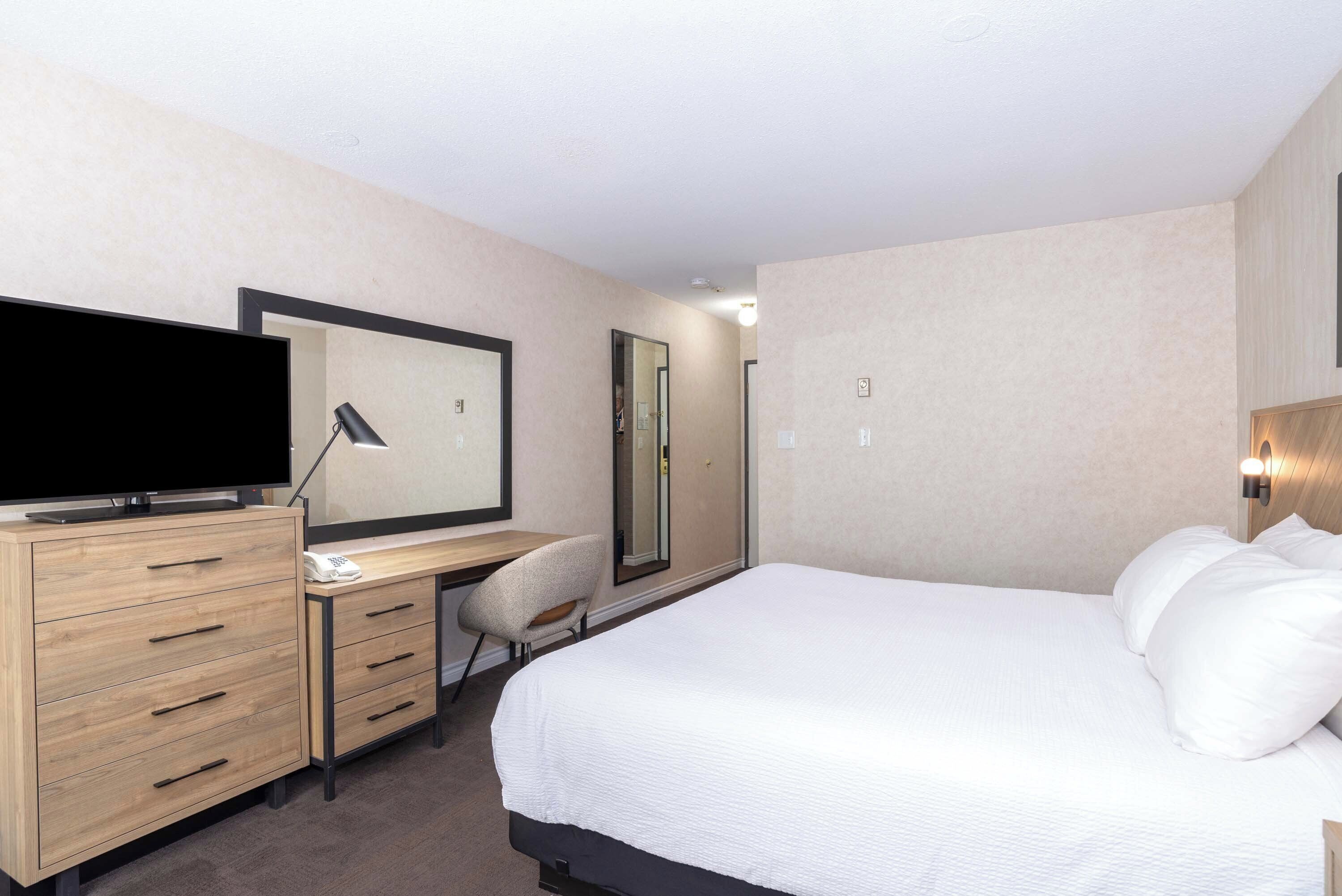 Habitación de hotel con una cama, un escritorio con televisor de pantalla plana, una silla y un espejo.