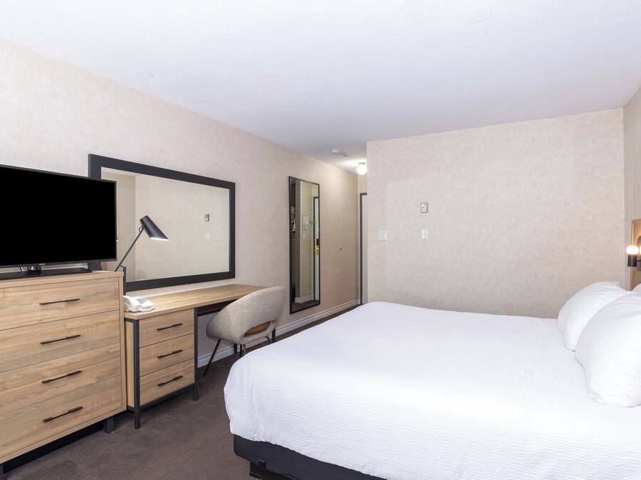 A hotel room with a bed, a desk with a flat-screen TV, a chair, and a mirror.