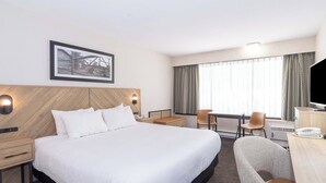 Habitació d'hotel amb un llit gran, una taula de treball amb una cadira, una televisió i un quadre al mur.