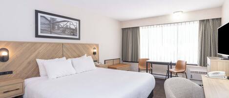 Een hotelkamer met een groot bed, een bureau met stoel, een televisie en een lijst aan de muur.