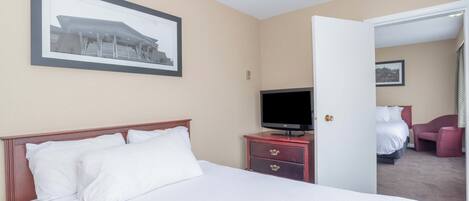 A hotel room with a bed, a television on a dresser, a framed picture on the wall, and a door leading to another room.