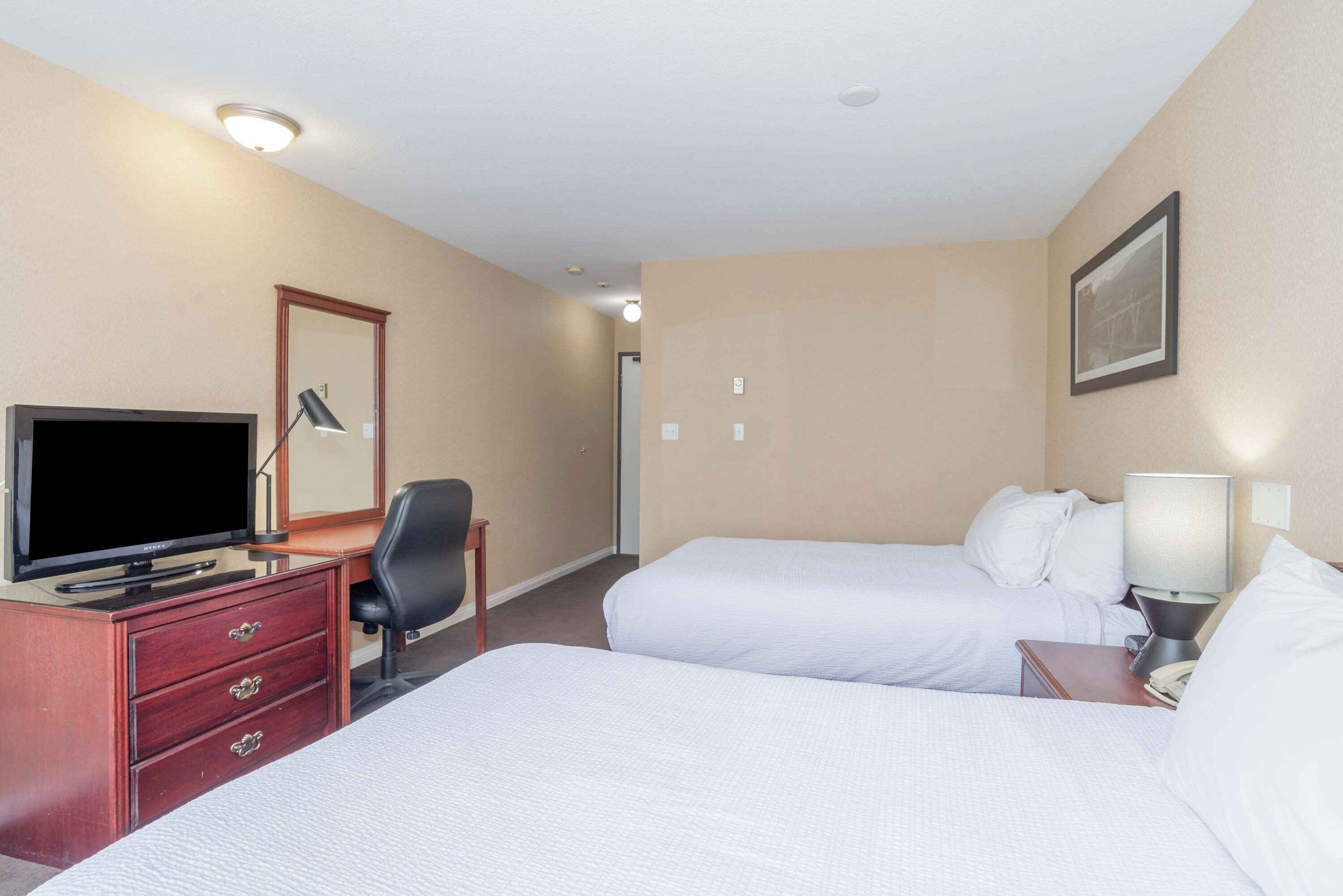 Une chambre d’hôtel avec deux lits, un bureau avec une télévision, une chaise et une table de chevet avec une lampe.