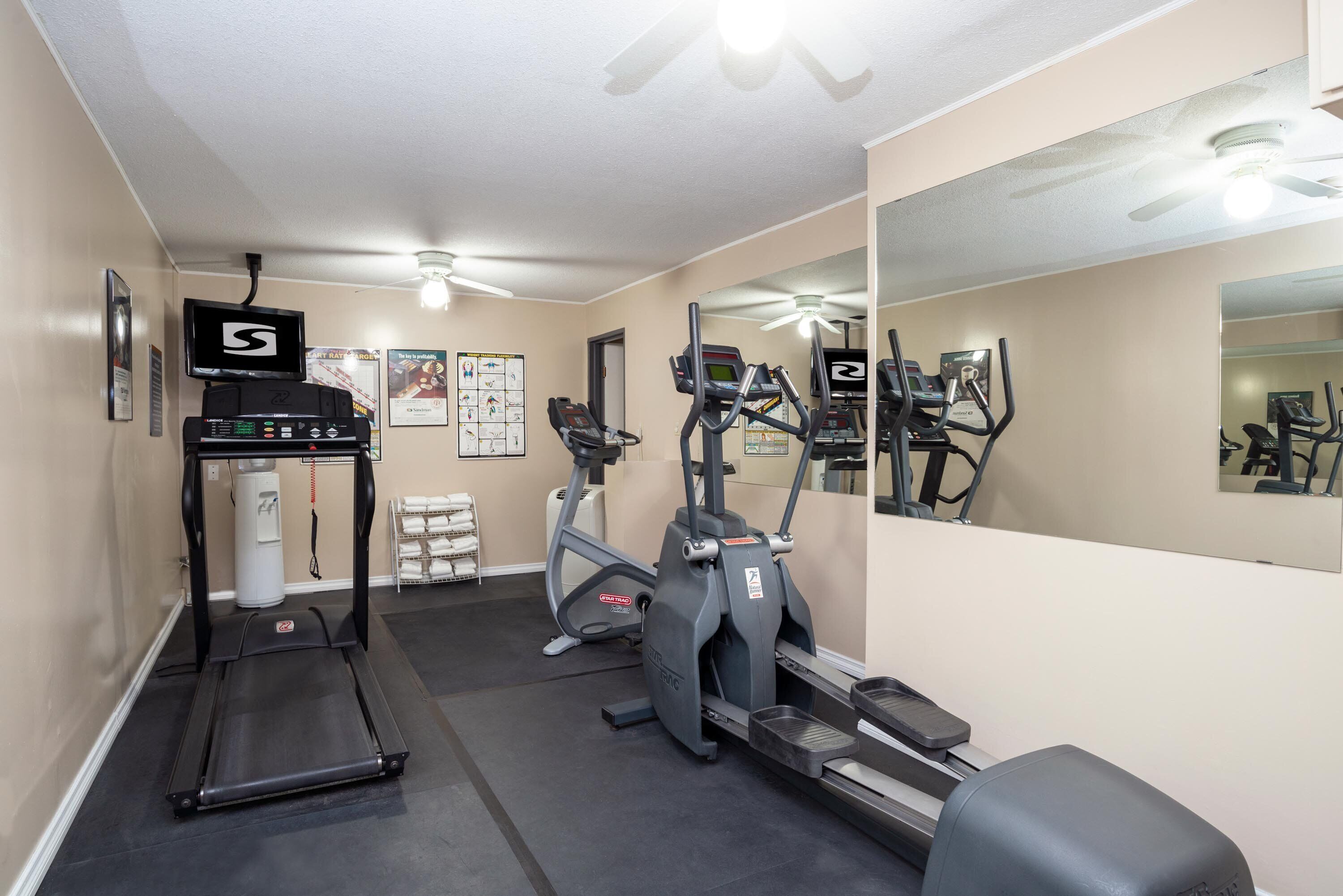 A gym with treadmills, elliptical machines, and a mirrored wall.