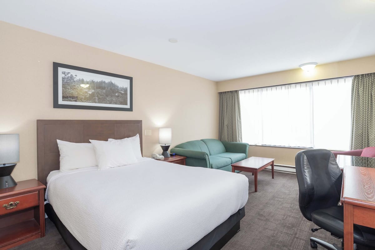 Habitación de hotel con una cama grande, un escritorio, una silla, una mesita, una lámpara y un cuadro en la pared.