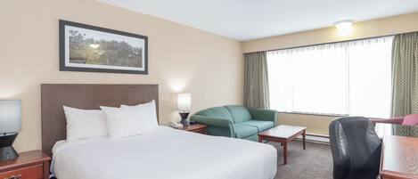 Hotelkamer met een groot bed, een bureau, een stoel, een kleine tafel, een lamp en een lijst aan de muur.