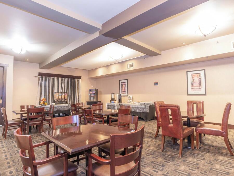 Une salle à manger d’hôtel avec plusieurs tables et chaises, un tapis à motifs et des poutres apparentes au plafond.