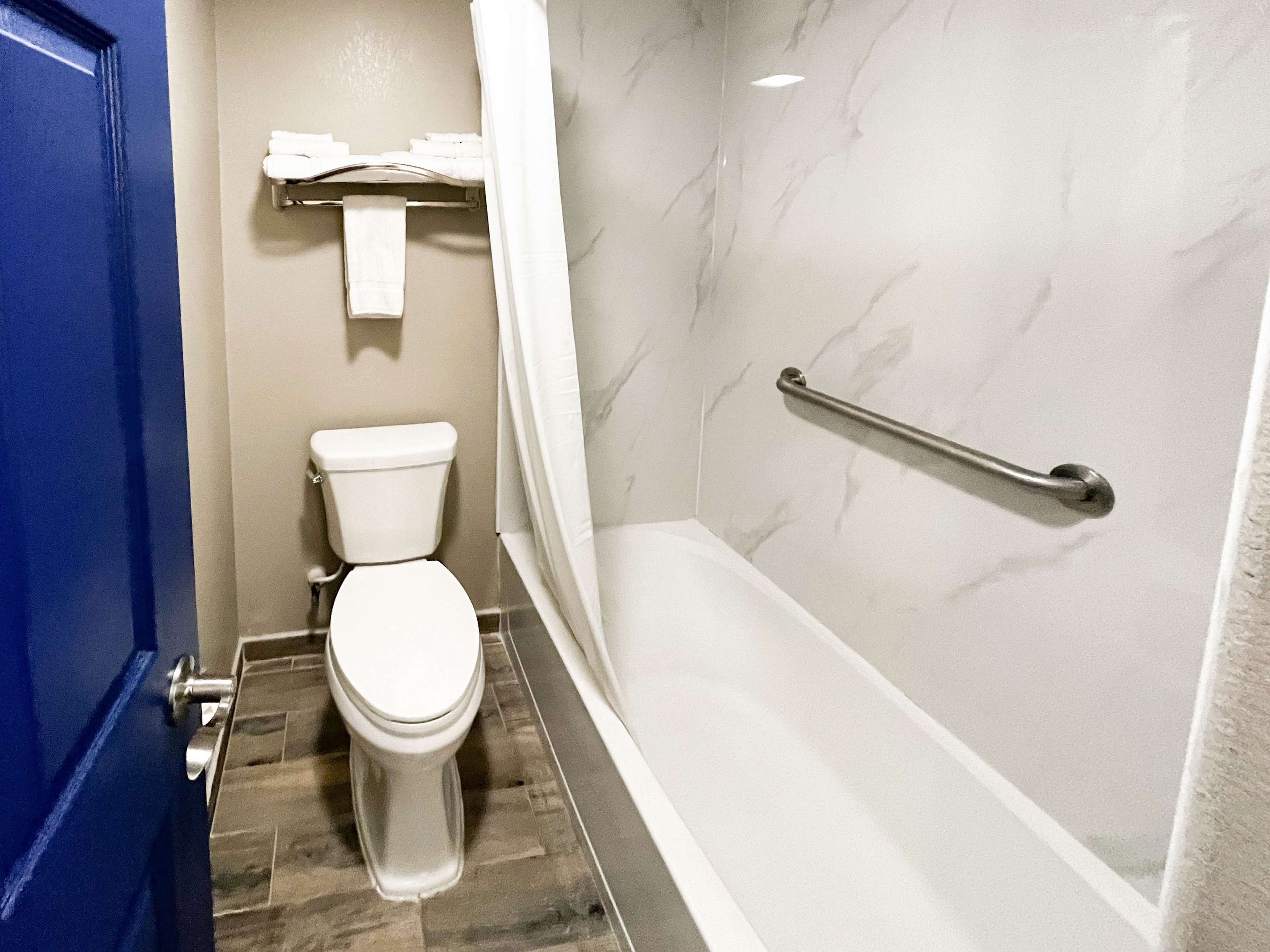 A bathroom with a toilet, a shower with a grab bar, and a towel rack.