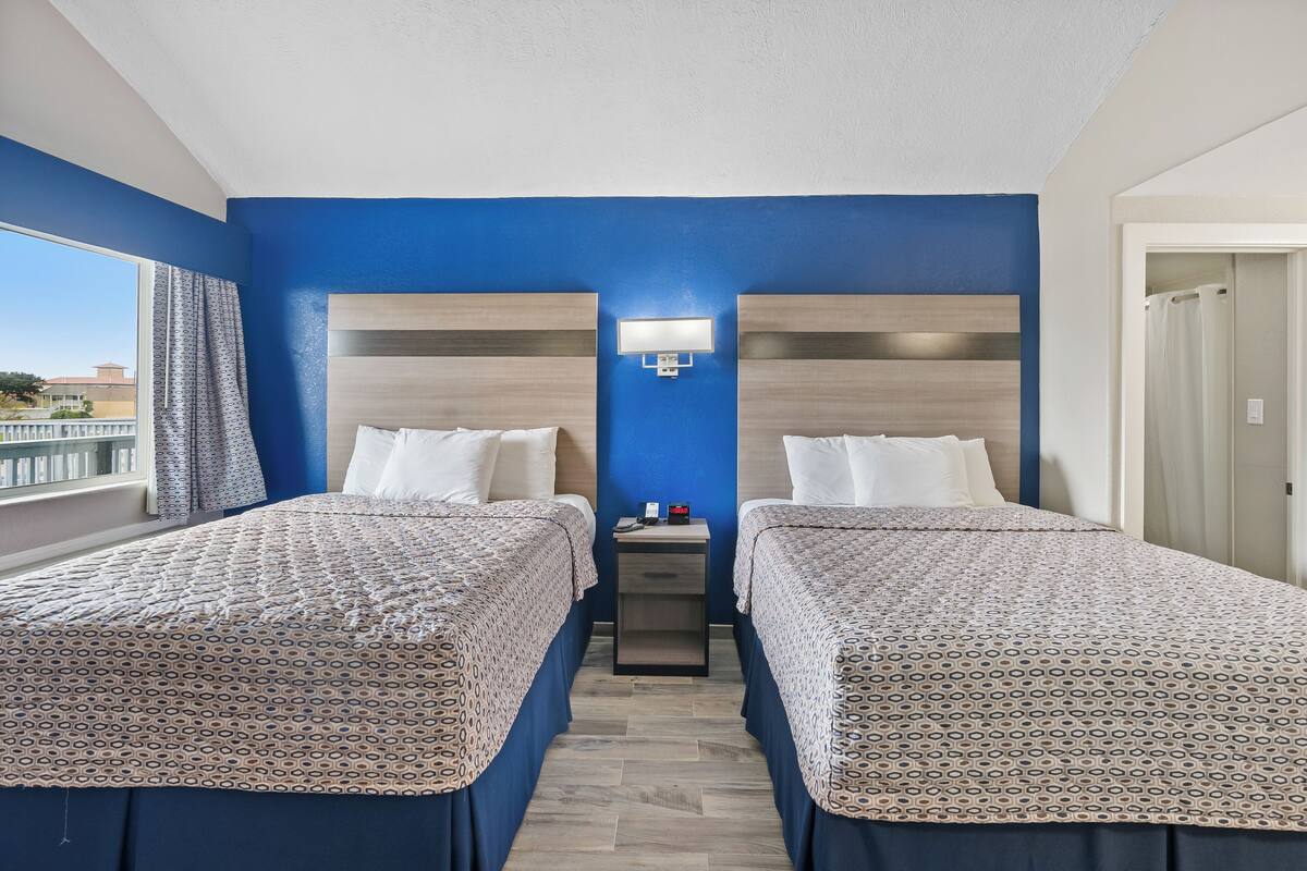 Habitación de hotel con dos camas, una mesita de noche y una ventana con vistas.