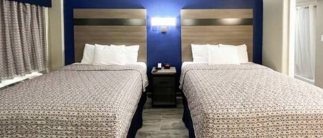 A hotel room with two beds, a nightstand, and a wall-mounted light.