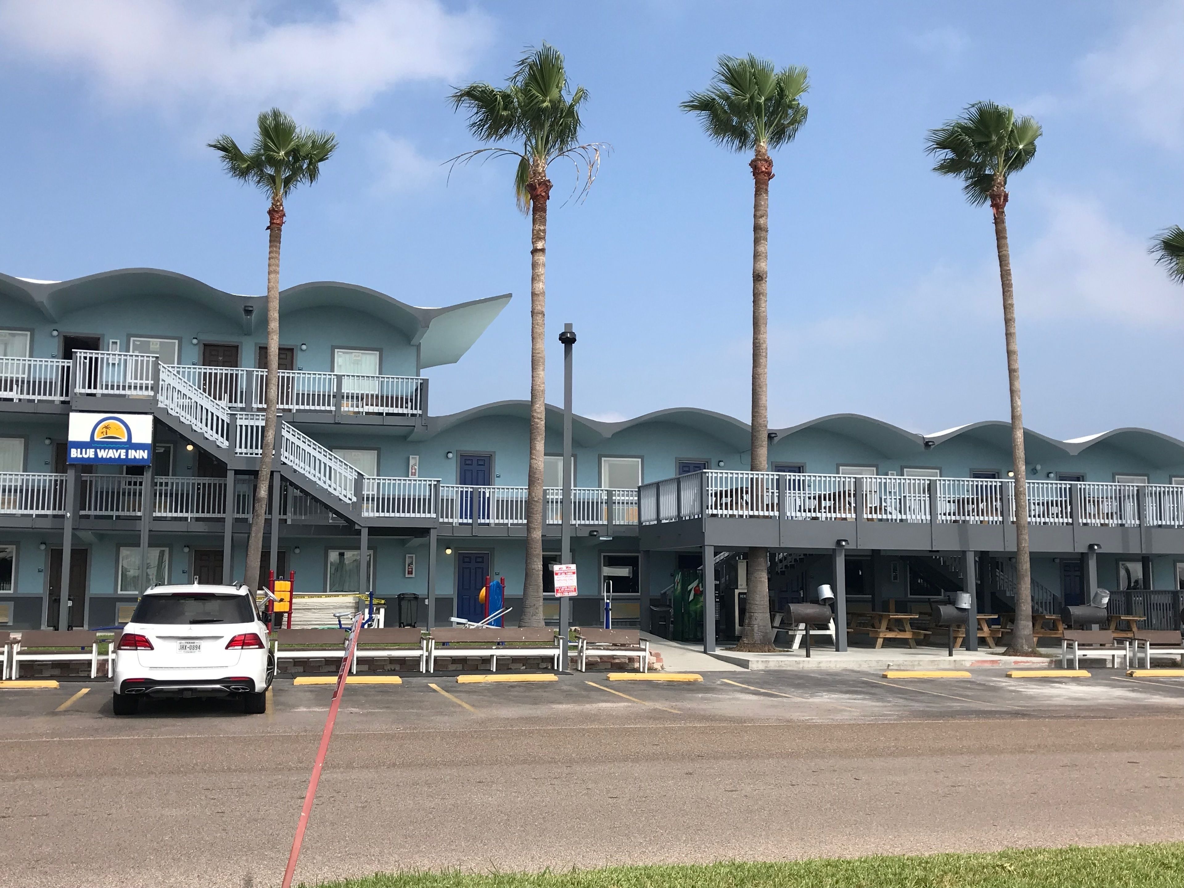 A hotel with a blue wave-like facade, multiple balconies, and palm trees.