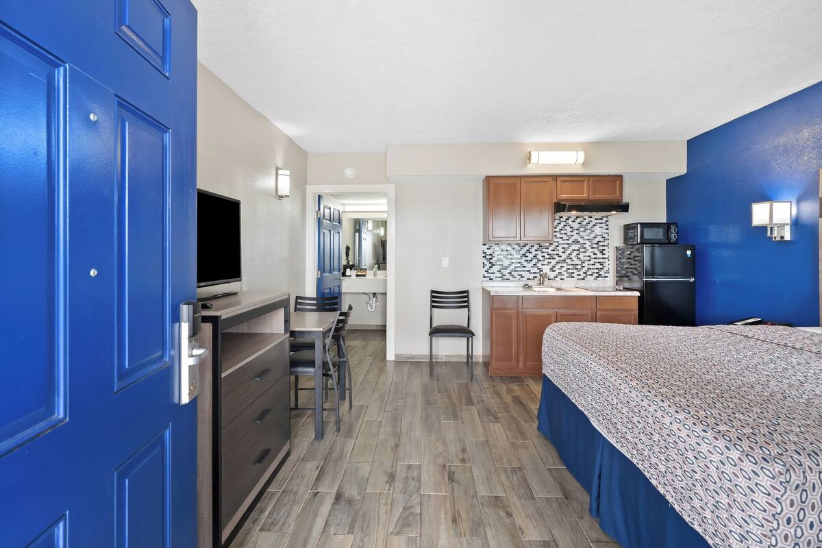 Una habitación de hotel compacta con kitchenette, una cama, un escritorio y un televisor.