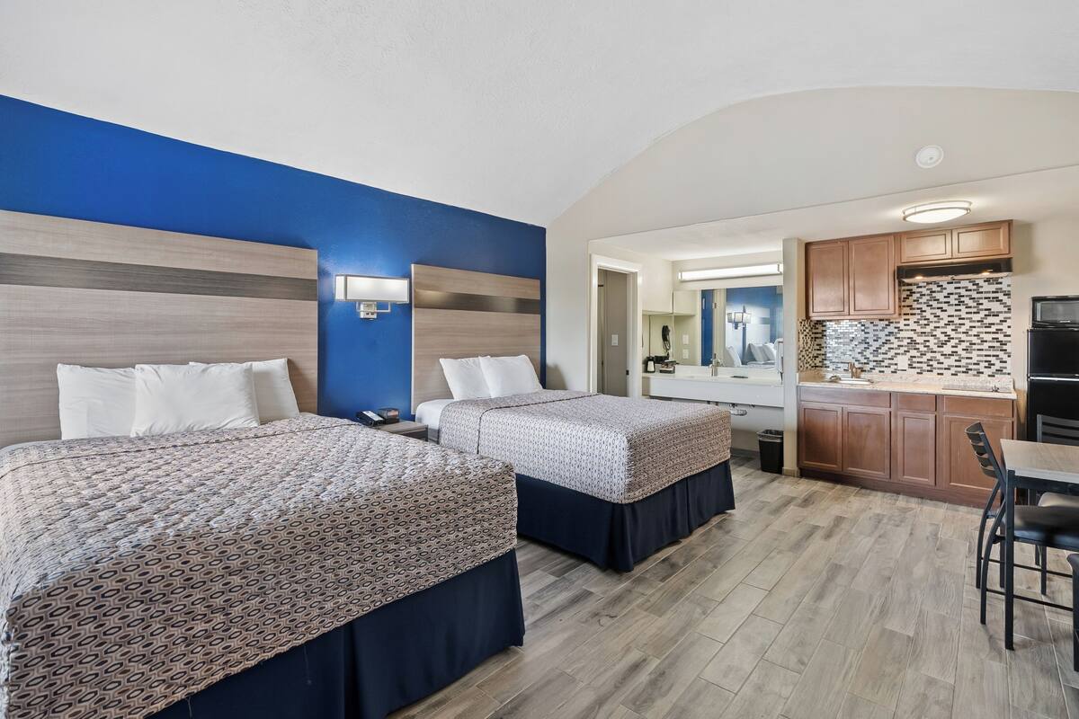 Una habitación de hotel con dos camas, una kitchenette y un baño visible a través de una puerta abierta.
