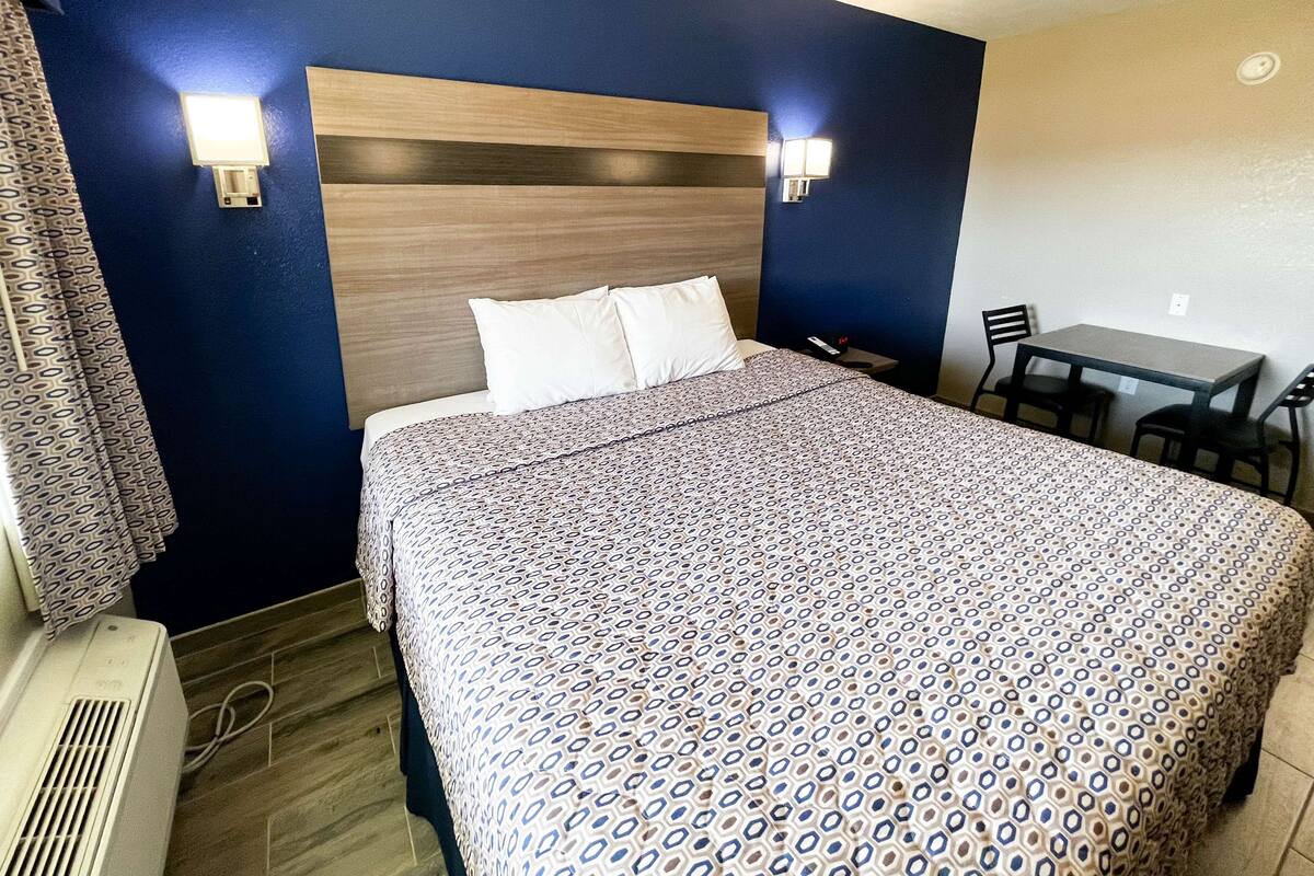 Habitación de hotel con una cama grande, cabecera de madera, dos lámparas de noche, un escritorio con una silla y una ventana con cortinas.