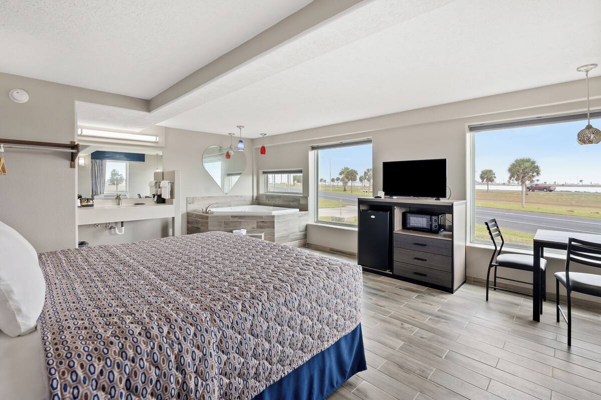 Una habitación de hotel moderna con una cama grande, un escritorio con televisor de pantalla plana, un tocador con espejo y vistas al exterior.