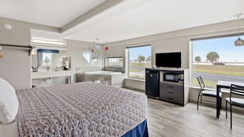 Una habitación de hotel moderna con una cama grande, un escritorio con televisor de pantalla plana, un tocador con espejo y vistas al exterior.