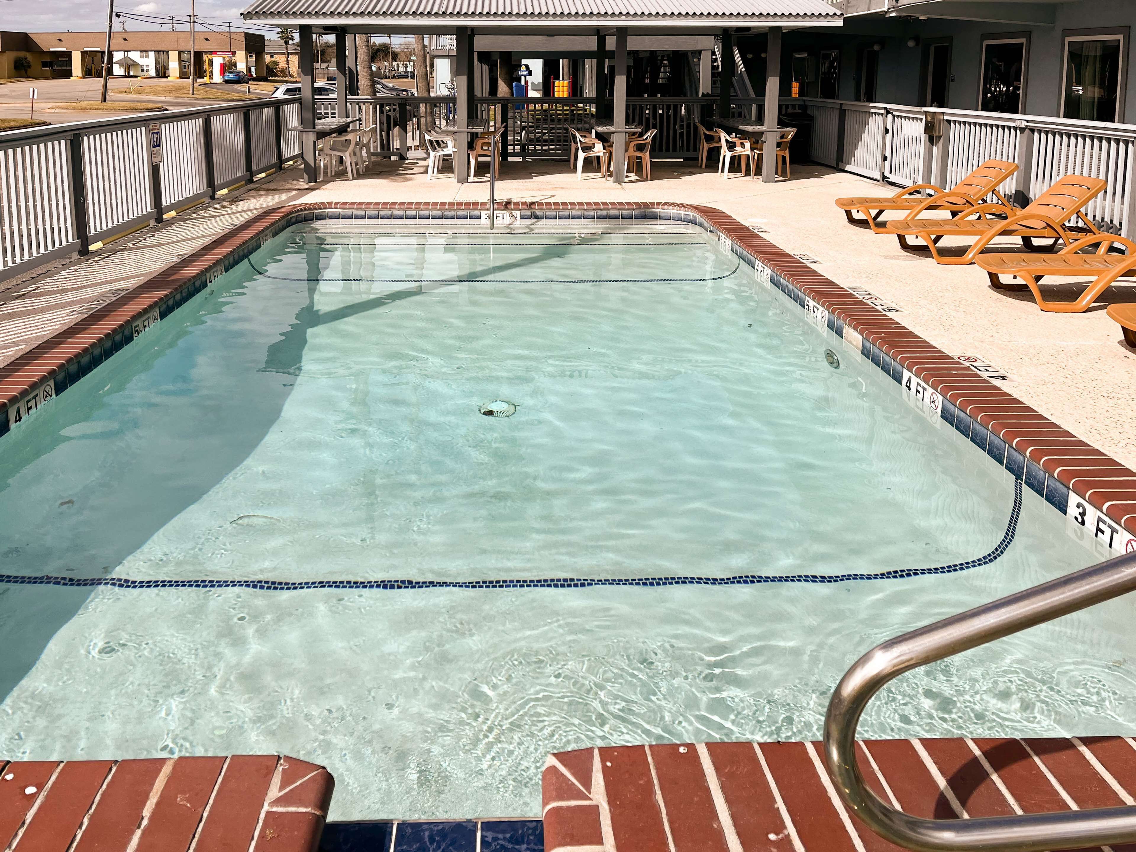 Une piscine aux eaux cristallines, bordée de carreaux, entourée d’une terrasse aménagée avec des chaises et des tables.