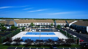 Un complexe sportif comprenant un court de tennis, un parking et des bâtiments à plusieurs étages dotés d’un toit en pente.