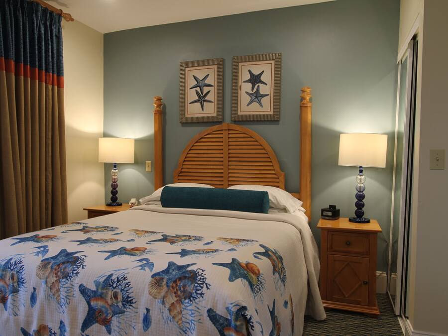 A hotel room with a bed, two wall-mounted starfish decorations, a wooden headboard, two bedside tables with lamps, and a window with curtains.