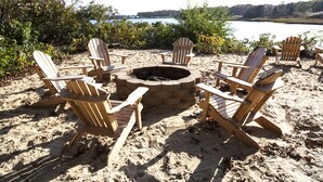 Un espace aménagé avec des sièges au bord de la plage, comprenant des fauteuils Adirondack disposés autour d’un foyer en pierre.