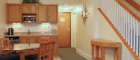 A compact kitchen with wooden cabinets, a microwave, and a dining area with a table and chairs.
