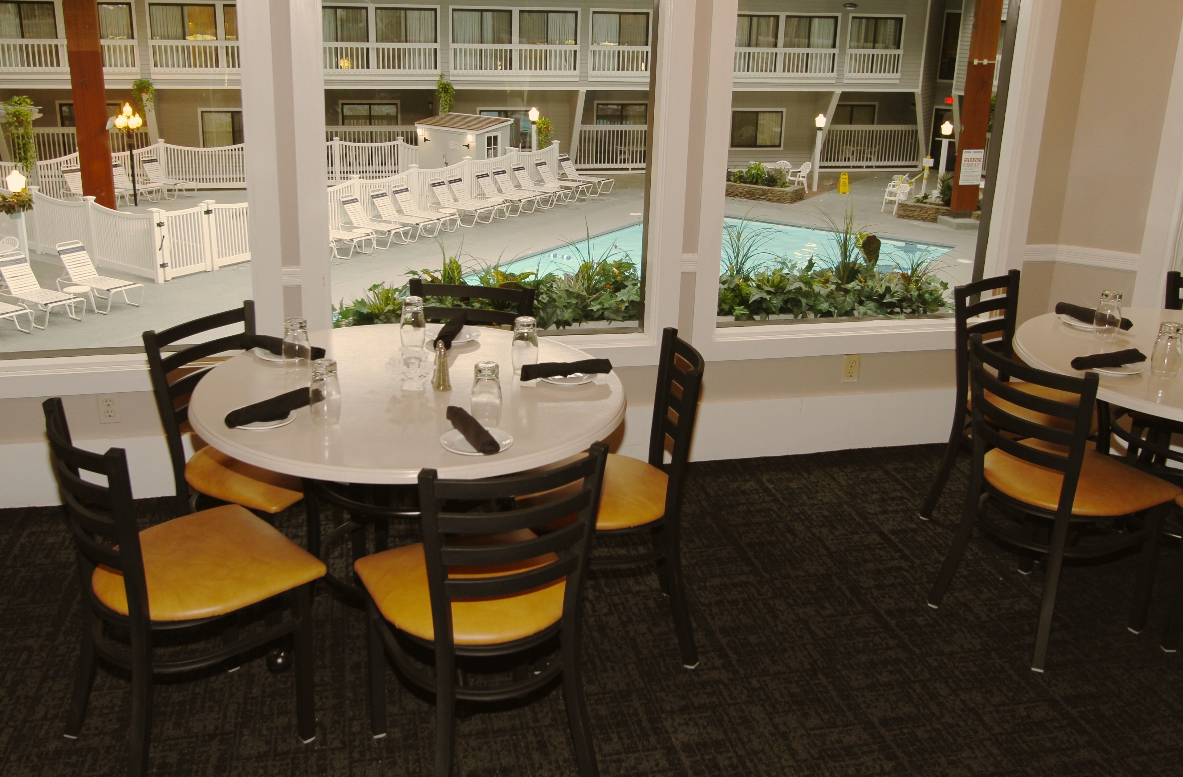 A dining area with round tables and chairs, a view of a pool and outdoor seating.