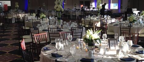 A banquet hall with round tables set for a formal event, featuring white tablecloths, chairs, and floral centerpieces.