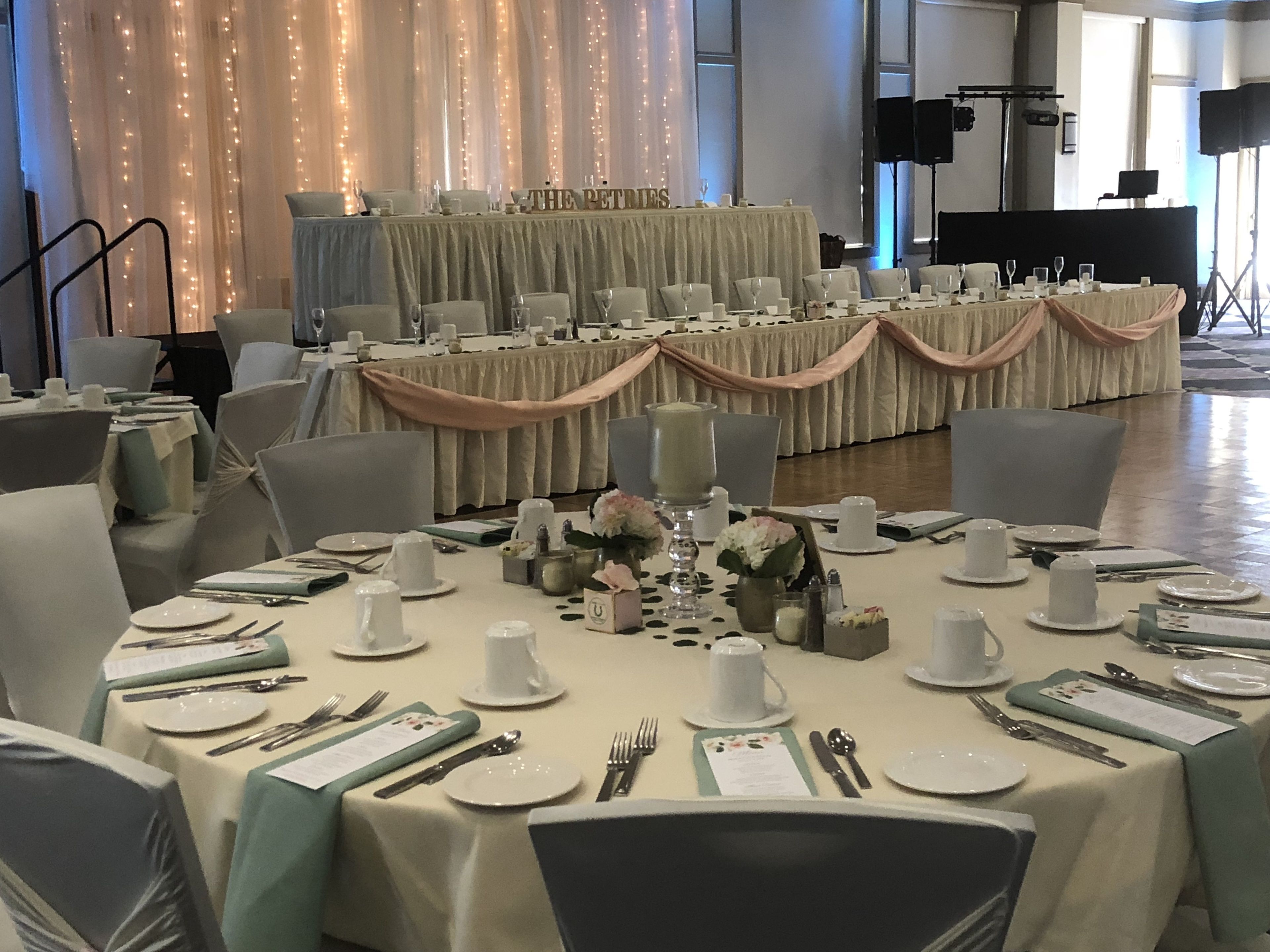 Une salle de banquet avec des tables rondes dressées pour un événement formel, agrémentée de nappes blanches, de compositions florales et de couverts disposés avec soin.