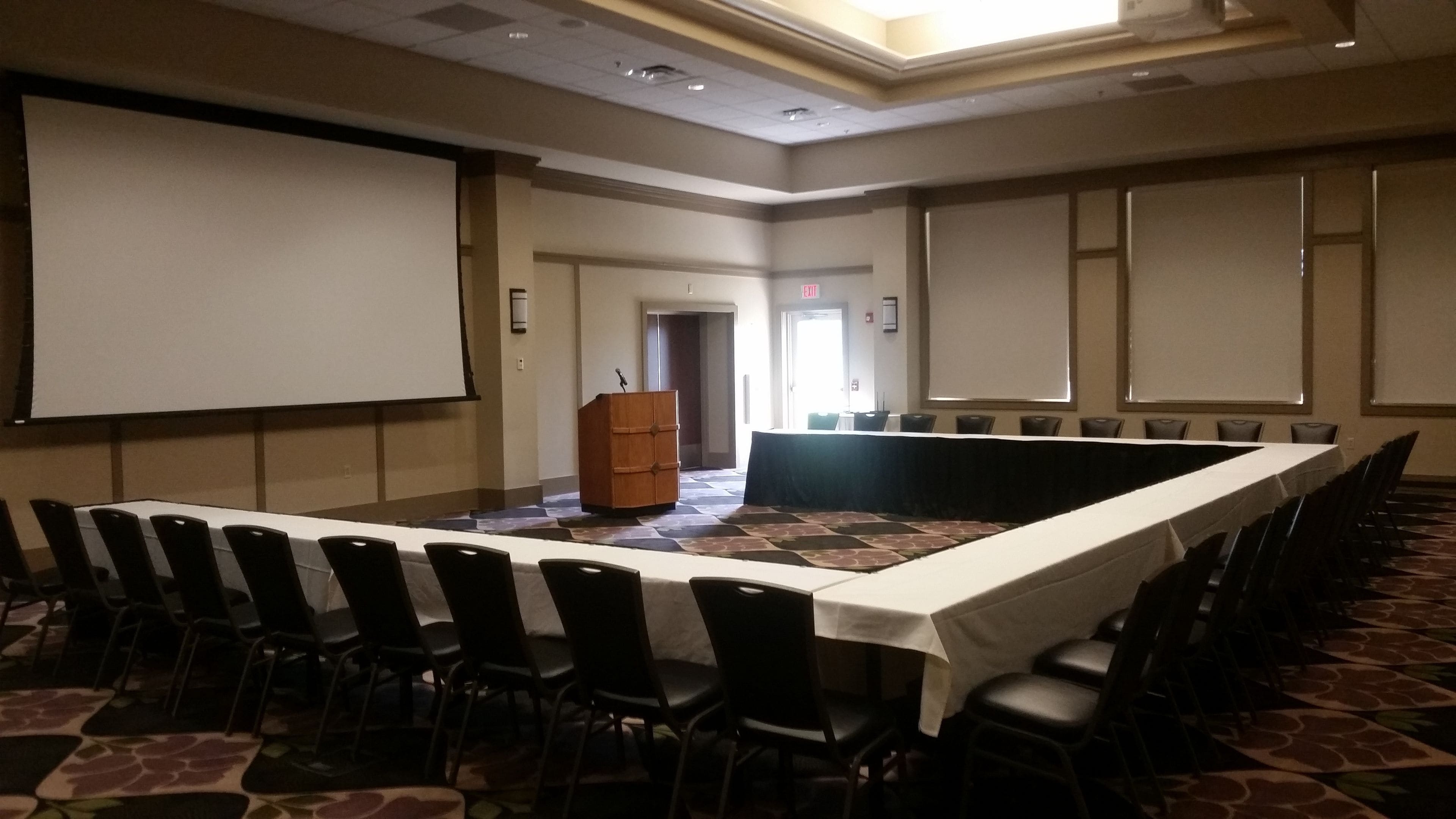 A conference room with a long table, chairs, a podium, and a projector screen.