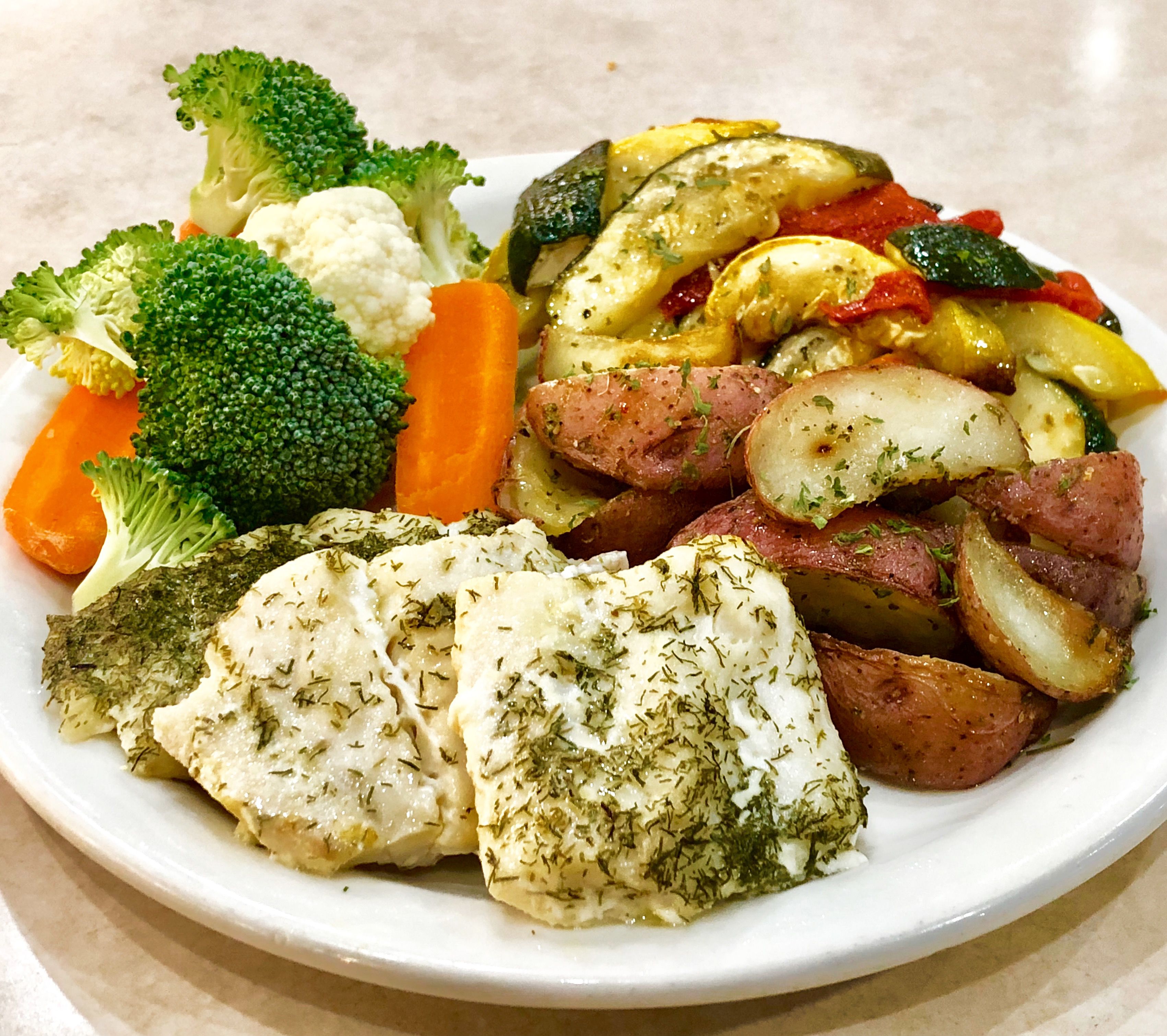 Un plato de comida con diferentes verduras y un trozo de pescado.