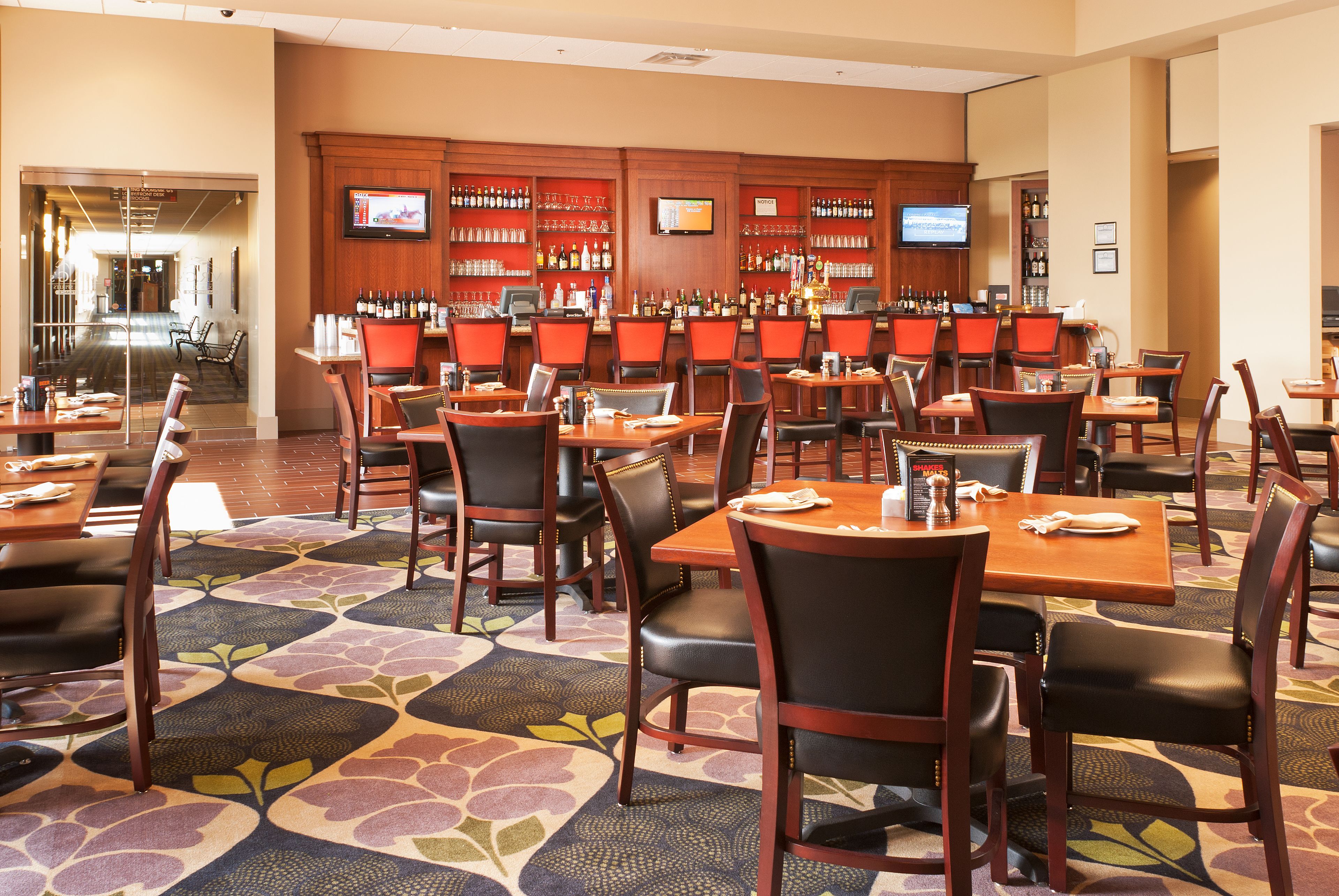 A restaurant with multiple tables and chairs, a bar area with shelves of bottles, and a television mounted on the wall.