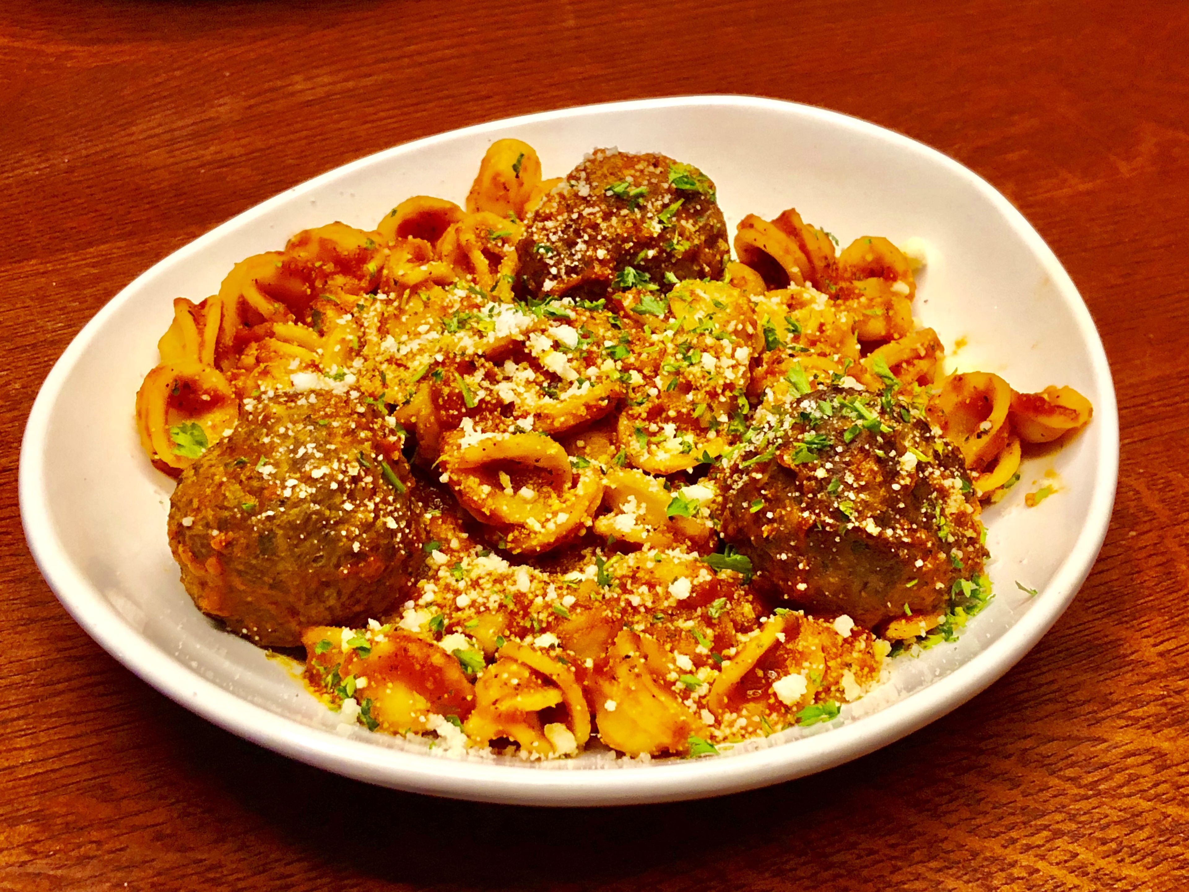A plate of pasta with meatballs and squid rings, garnished with herbs and cheese.