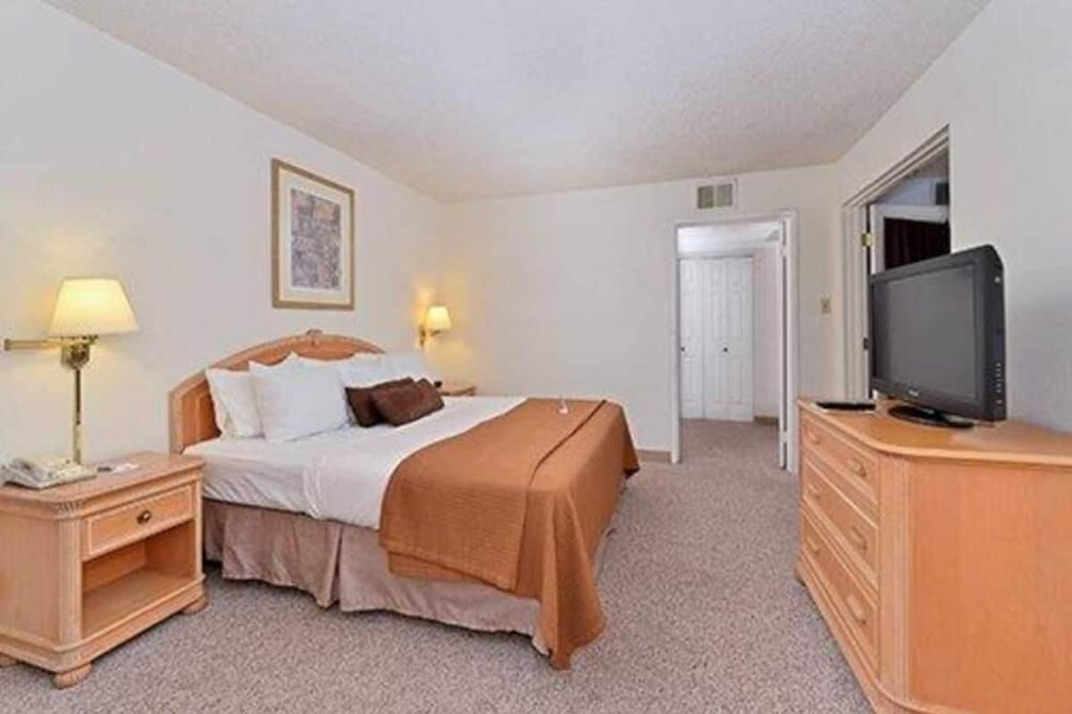 Une chambre d’hôtel avec un lit, des lampes de chevet, une télévision, une commode et une porte.