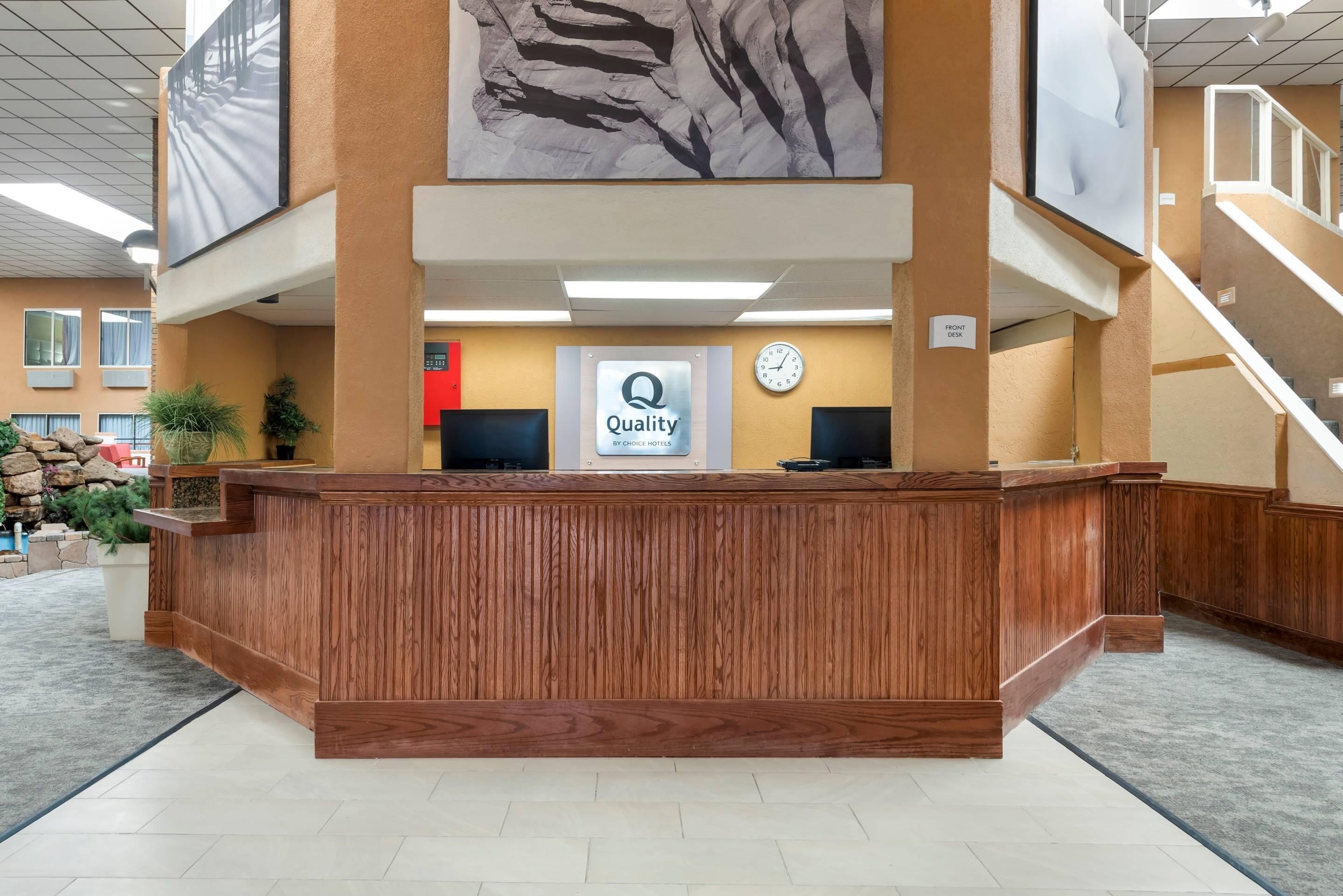 A reception desk with a 'Quality by Choice Hotels' sign, a clock, and a staircase.