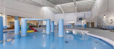 An indoor swimming pool with blue pillars, a slide, and a clear ceiling.