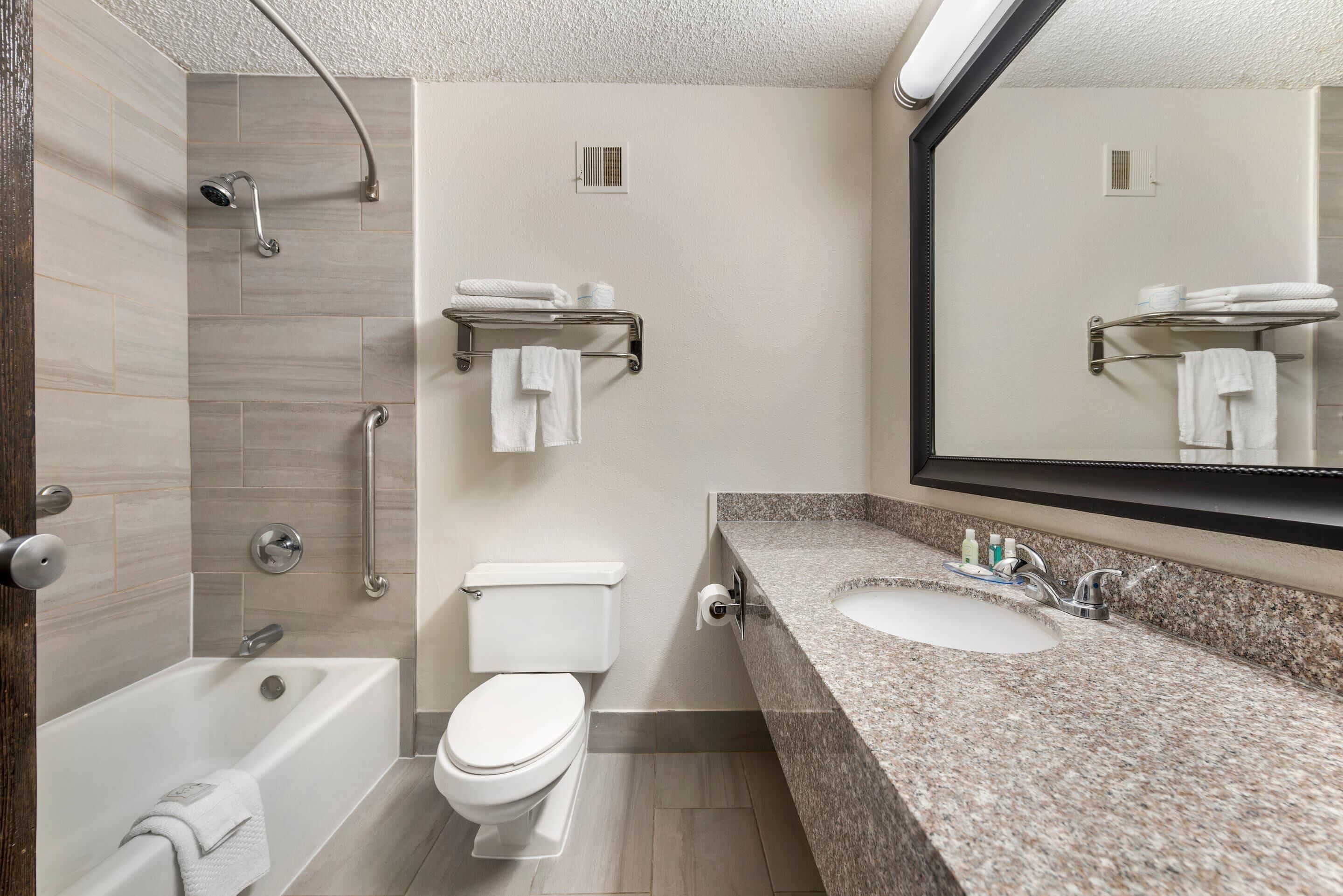 A modern bathroom with a bathtub, toilet, and sink, featuring a large mirror and towel racks.