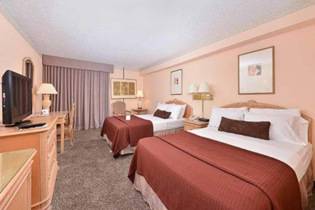 Une chambre d’hôtel avec deux lits, un bureau avec une télévision et une fenêtre avec des rideaux.