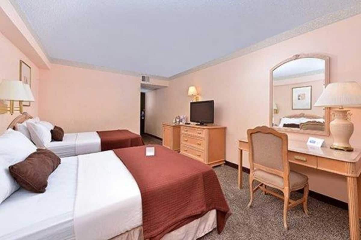 Une chambre d’hôtel avec deux lits, un bureau, une chaise, une télévision et un miroir.