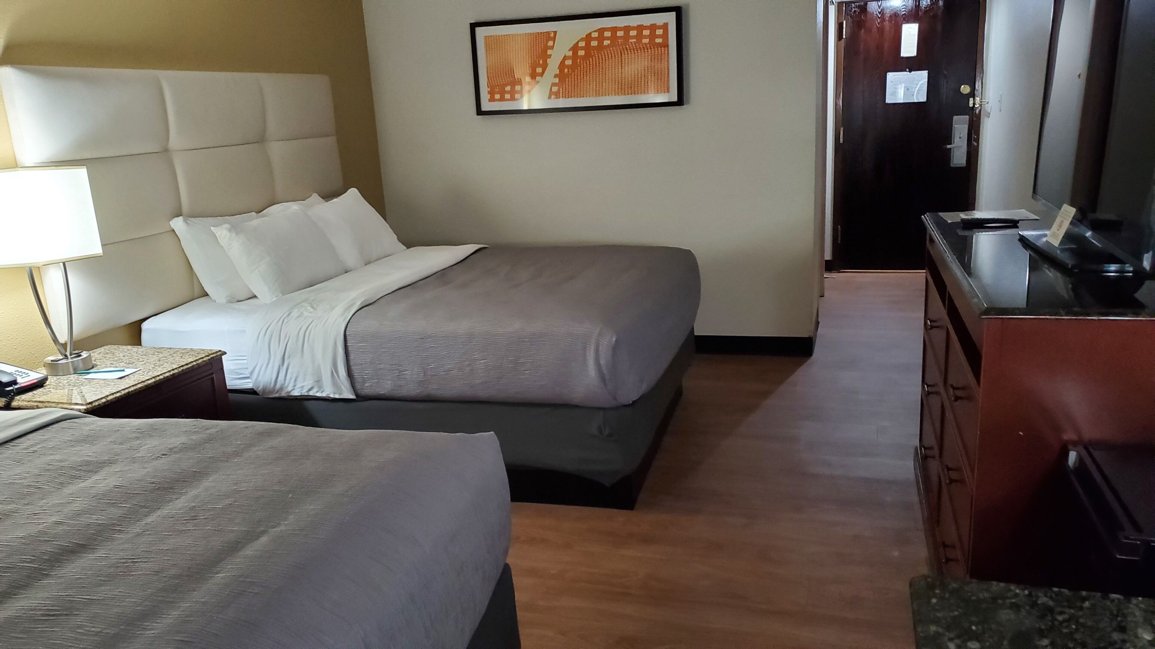 A hotel room with two beds, a desk with a lamp, a framed picture on the wall, and a dresser.