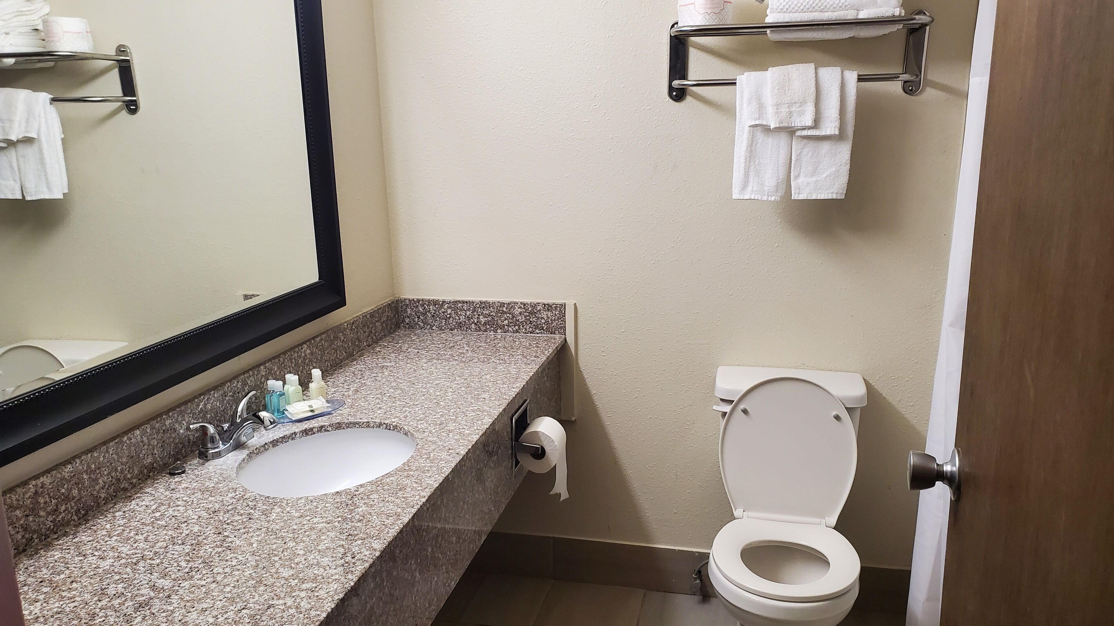 Ein Badezimmer mit Granitplatte, einem weißen Waschbecken, einem Spiegel, einer Toilette und Handtuchhaltern.