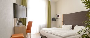 A hotel room with a bed, a desk with a chair, a TV, and a bedside table with a lamp. - Apartmenthotel Kaiser Karl (  Self-check-in )  (Bonn)