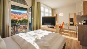 A hotel room with a bed, a TV, a desk, and a balcony with a view of flowers. - Apartmenthotel Kaiser Karl (  Self-check-in )  (Bonn)