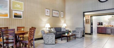 A hotel lobby with a dining area, sofas, and a kitchen visible through an open door.