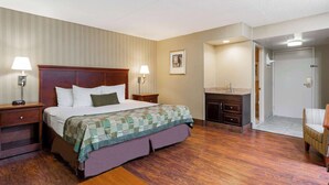 A hotel room with a wooden bed, two bedside tables with lamps, a small dresser, a bathroom with a sink, and a chair. - Days Inn by Wyndham Westminster (Westminster)