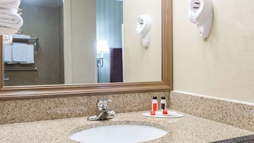 Baño de hotel con lavamanos de encimera de granito, un espejo grande, un perchero con toallas dobladas y un secador de manos montado en la pared.