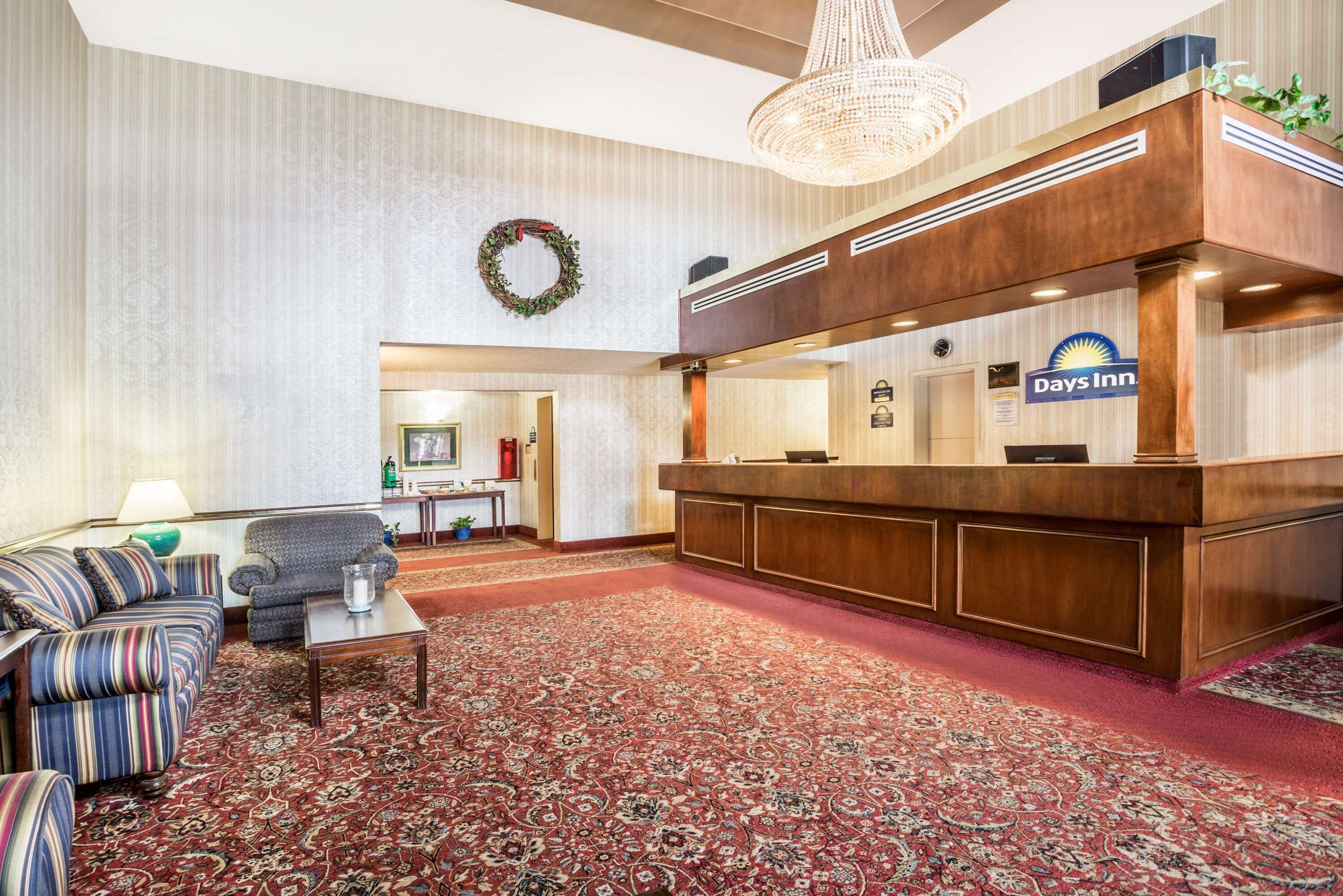 A hotel lobby with a reception desk, a striped sofa, a small table, and a patterned carpet.