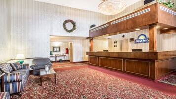 A hotel lobby with a reception desk, a striped sofa, a small table, and a patterned carpet.