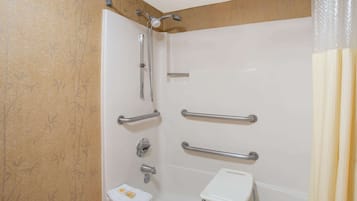 A bathroom with a shower, grab bars, a toilet, and a small sink.