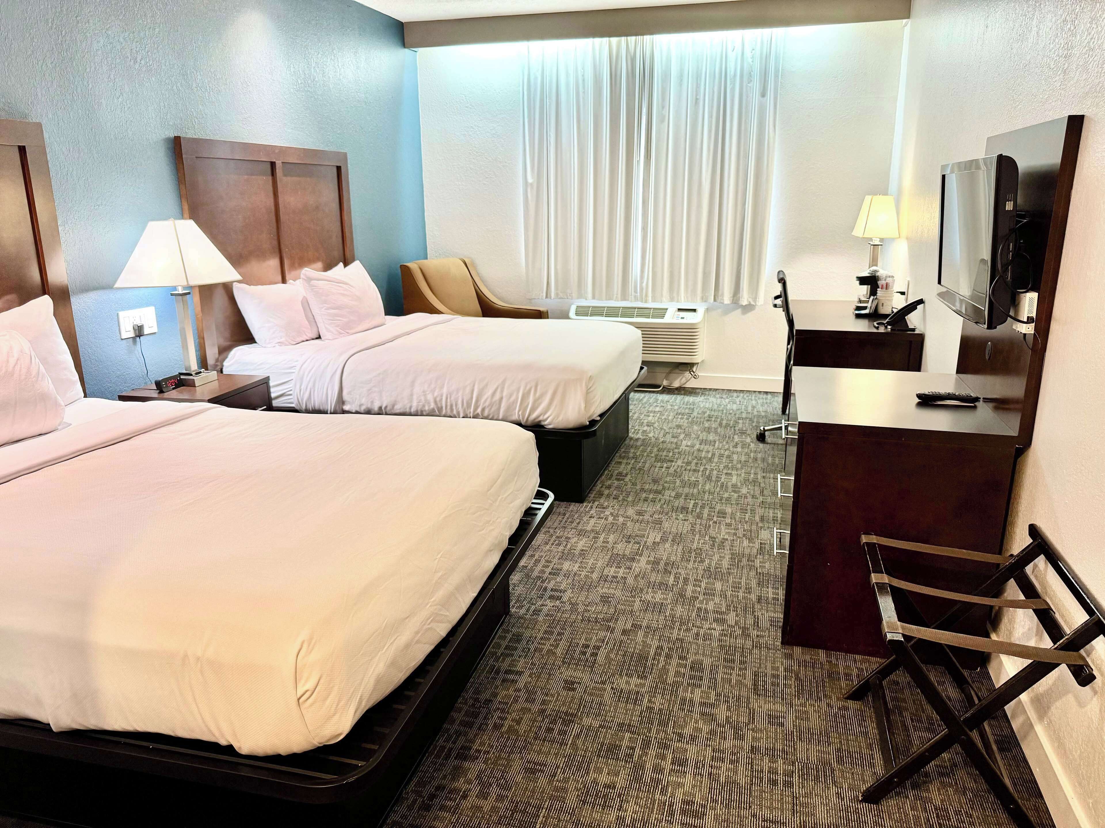 Une chambre d’hôtel avec deux lits, un bureau avec un ordinateur, une télévision et une chaise.