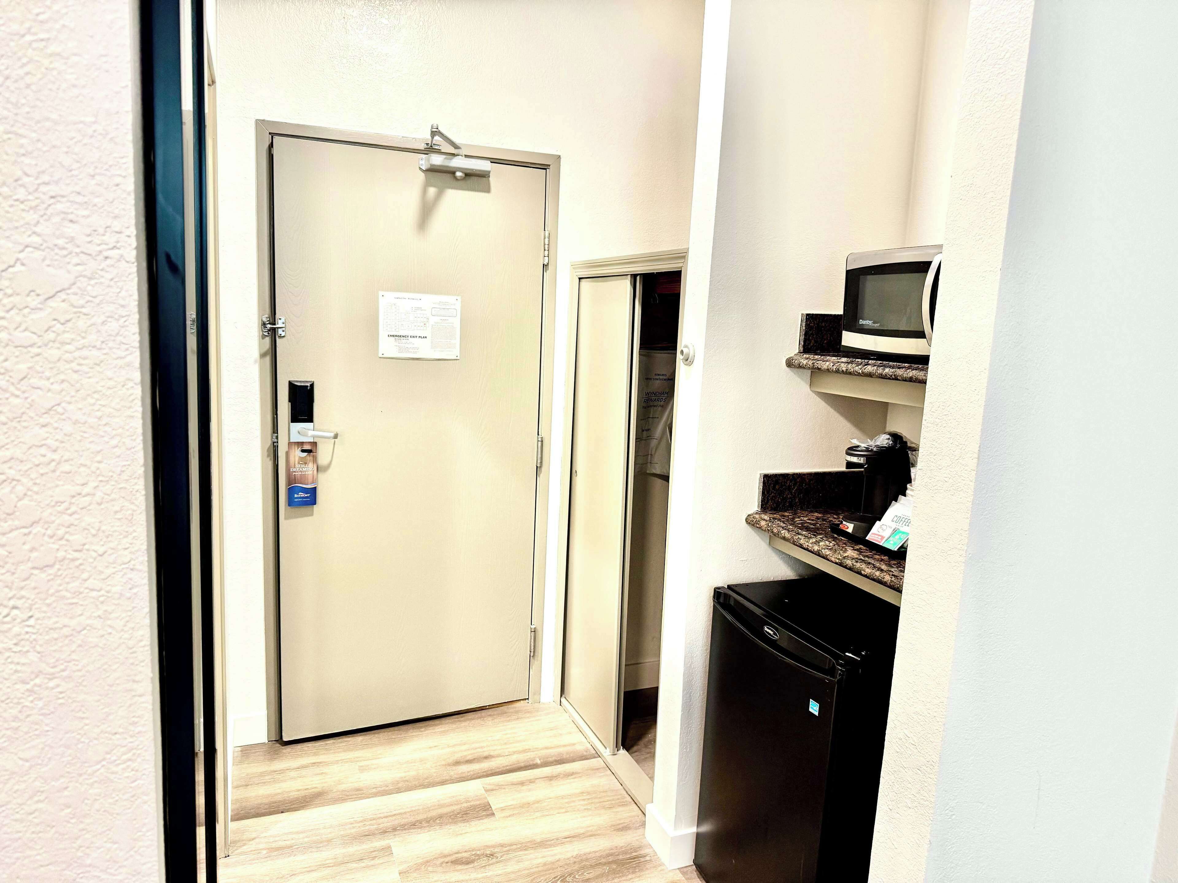 A narrow hallway with a beige door, a microwave on a shelf, and a black refrigerator.