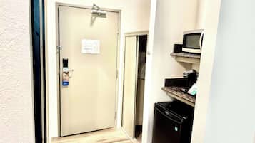A narrow hallway with a beige door, a microwave on a shelf, and a black refrigerator.